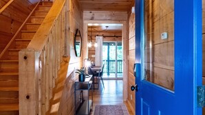 Interior de madera con una puerta azul, una escalera, un escritorio y una silla, y un ventanal.