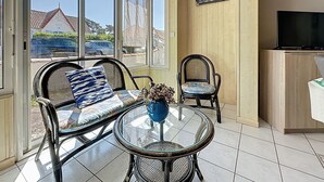 A sunlit room with a glass table, two wicker chairs, a sofa, and a television. - Ker Eric by Interhome (Tharon Plage)