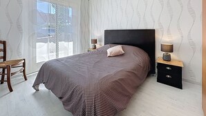 A bedroom with a bed, a nightstand, a chair, and a window with a view. - Ker Eric by Interhome (Tharon Plage)