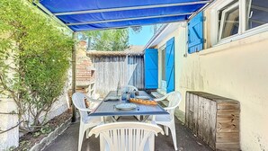 A covered patio with a table and chairs, a wooden fence, and a building with blue shutters. - Ker Eric by Interhome (Tharon Plage)