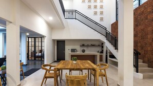 Un vaste espace dédié à la salle à manger, avec une table et des chaises en bois, une cuisine à l’arrière-plan et un escalier menant à un niveau supérieur.