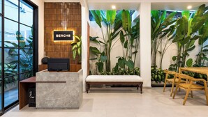 Un espace d’accueil avec un panneau indiquant « PLAGE », un comptoir de réception, un banc et un coin repas avec des chaises et des tables en bois.