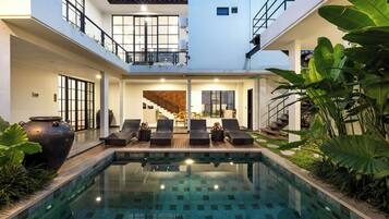 Un área de piscina moderna con sillones reclinables y vistas al interior.