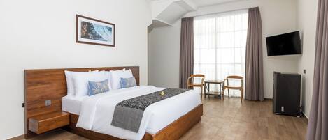 Quarto de hotel com cama de madeira, escrivaninha, cadeira, televisão e janela com cortinas.