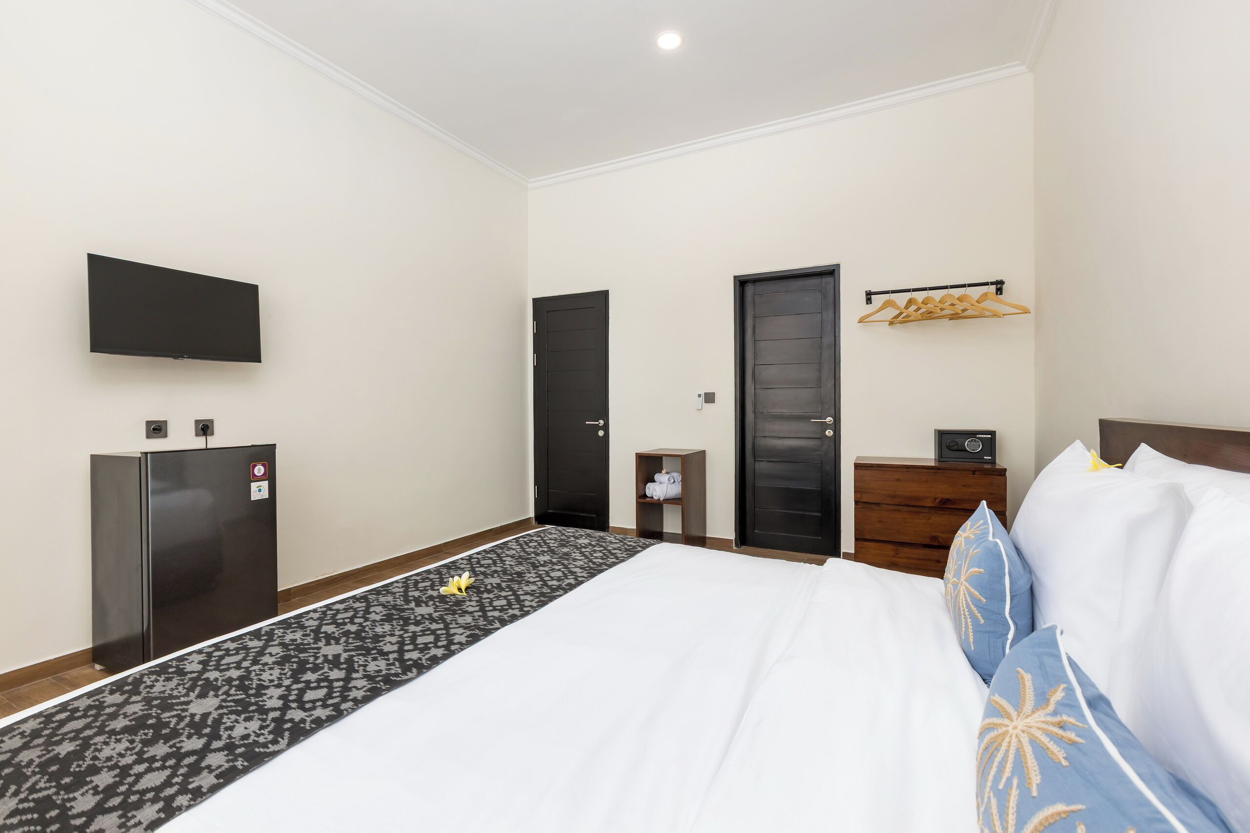A hotel room with a bed, a flat-screen TV, a wardrobe, a small table, and a coat rack.