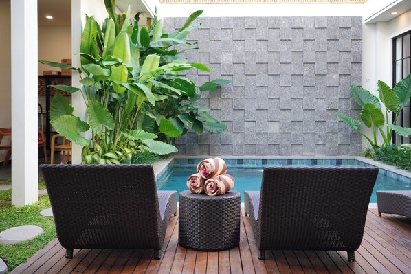 A poolside area with wicker chairs and a small round table with towels. - Beach8 Canggu By Kerta Living (Canggu)