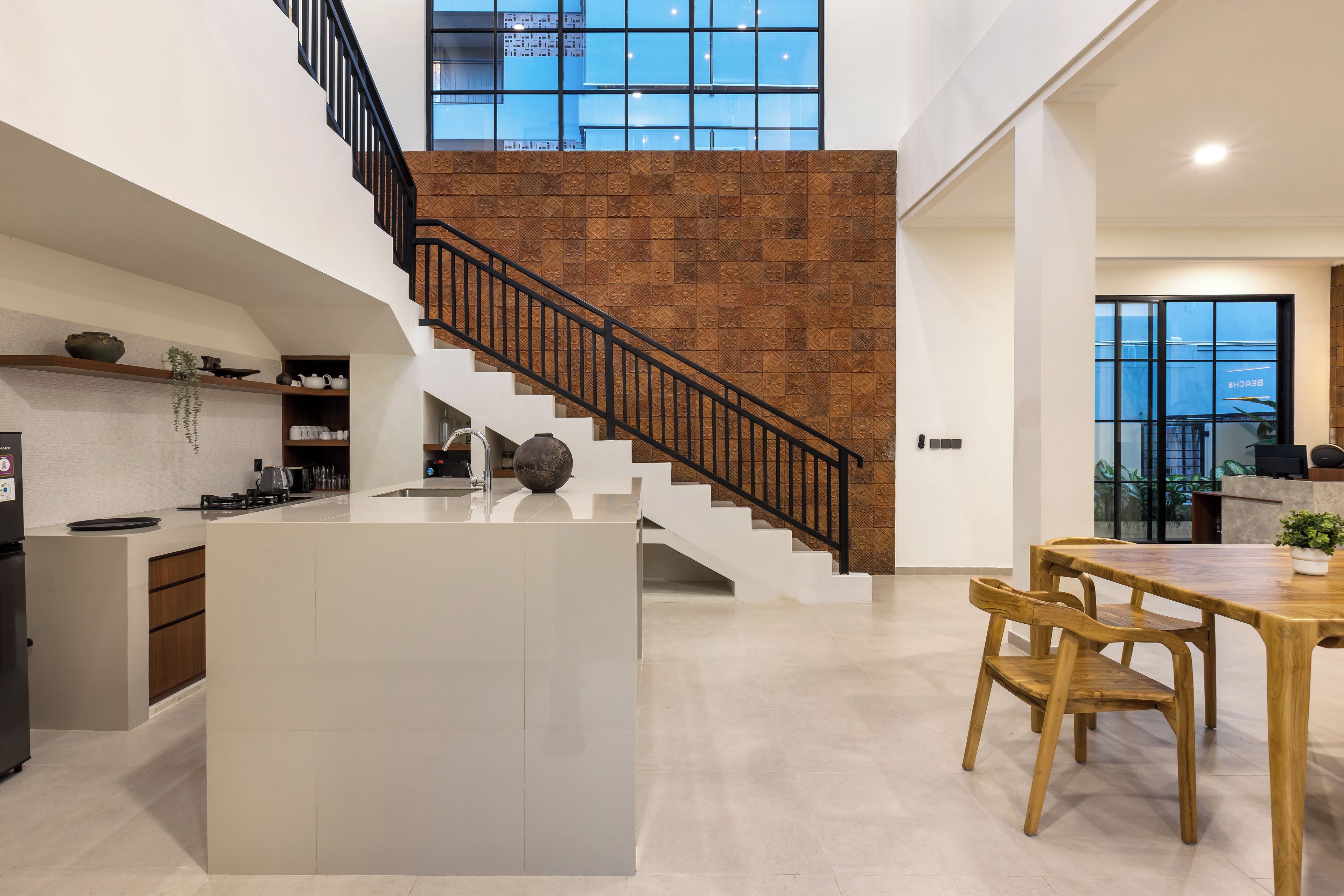 Una cocina moderna con una isla central, un área de comedor con sillas de madera y una escalera con barandilla negra.