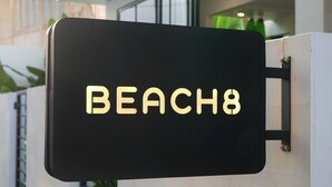 Un panneau noir portant l’inscription « BEACH8 » est fixé sur un mur blanc.