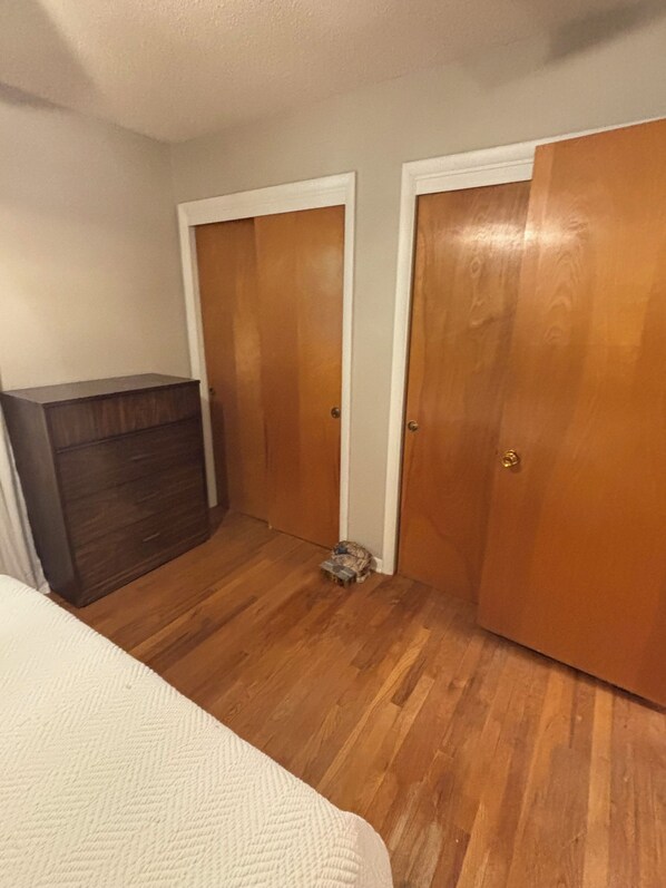 Un dormitorio con suelo de madera, un aparador y dos puertas.