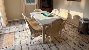 Een eetruimte met een witte tafel en rieten stoelen, een plafondventilator, een kast en een raam met gordijnen.