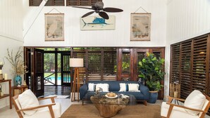 Ein geräumiges Wohnzimmer mit einem großen Sofa, zwei Holzstühlen, einem Couchtisch und einem Deckenventilator.