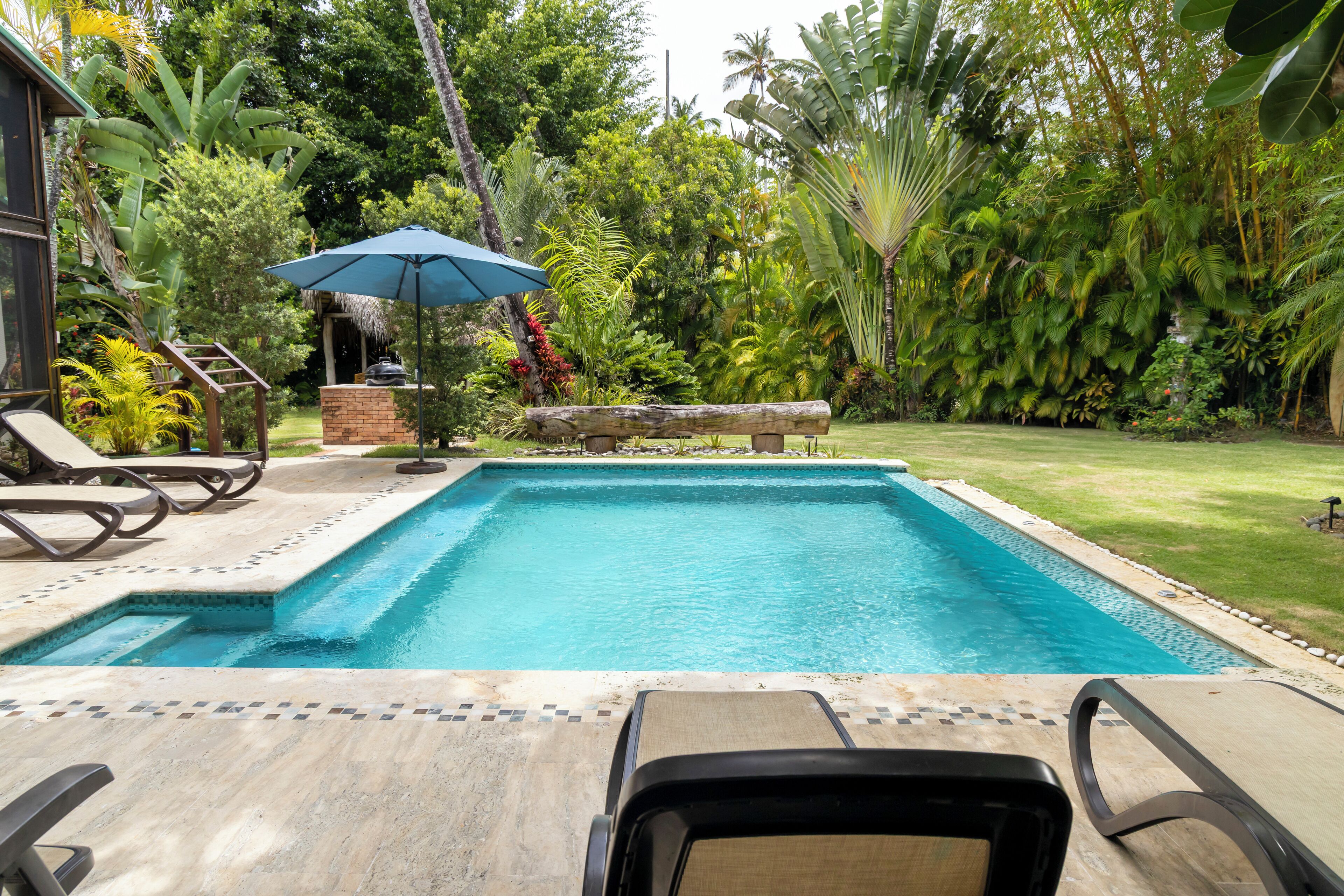 A swimming pool with lounge chairs and a thatched-roof structure.