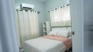 A bedroom with a bed, white curtains, a white headboard, and a white air conditioning unit. - Semi-detached newly renovated home in a friendly neighborhood (Las Piñas)