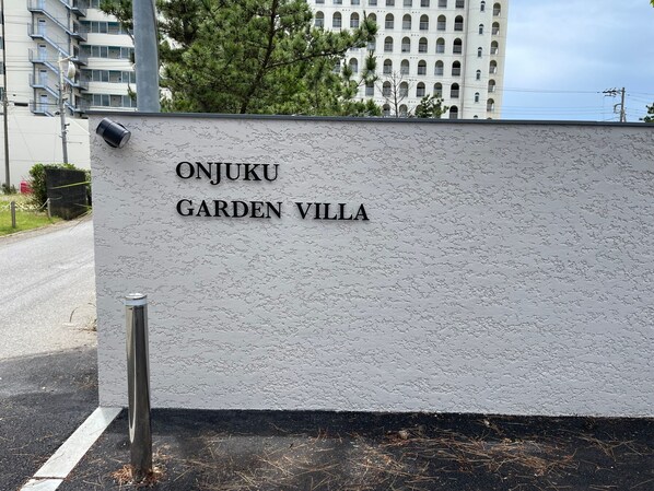 Une enseigne pour le complexe hôtelier Onjuku Garden Villa, avec un mur à texture et un poteau métallique.