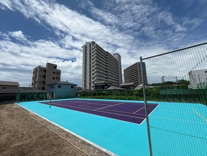 Un court de tennis en plein air, doté d’un filet, entouré de bâtiments et avec un ciel dégagé.