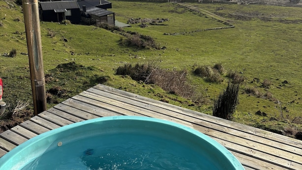 A hot tub on a wooden deck overlooking a beach with waves crashing and a rocky outcrop in the distance. - Tiny house Pilolcura (Valdivia)