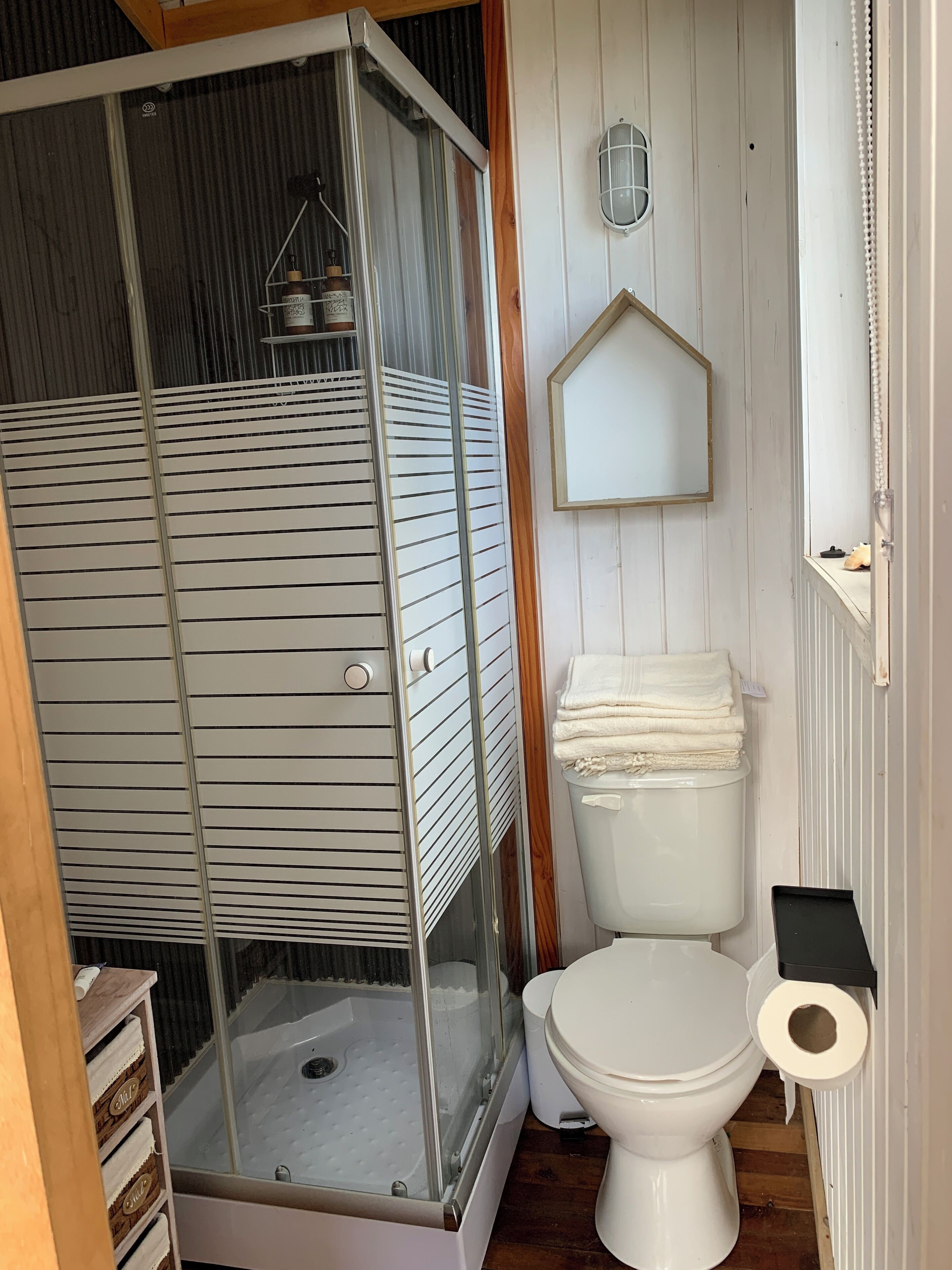Un baño con ducha de mampara de vidrio, inodoro y tocador de madera.