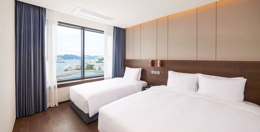A hotel room with two beds, a large window with a view of a cityscape, and a modern design with wooden paneling.