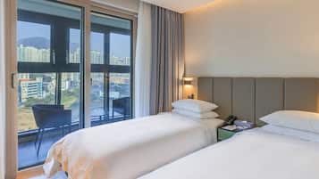 A hotel room with two beds, a nightstand, a chair, and a large window offering a city view.