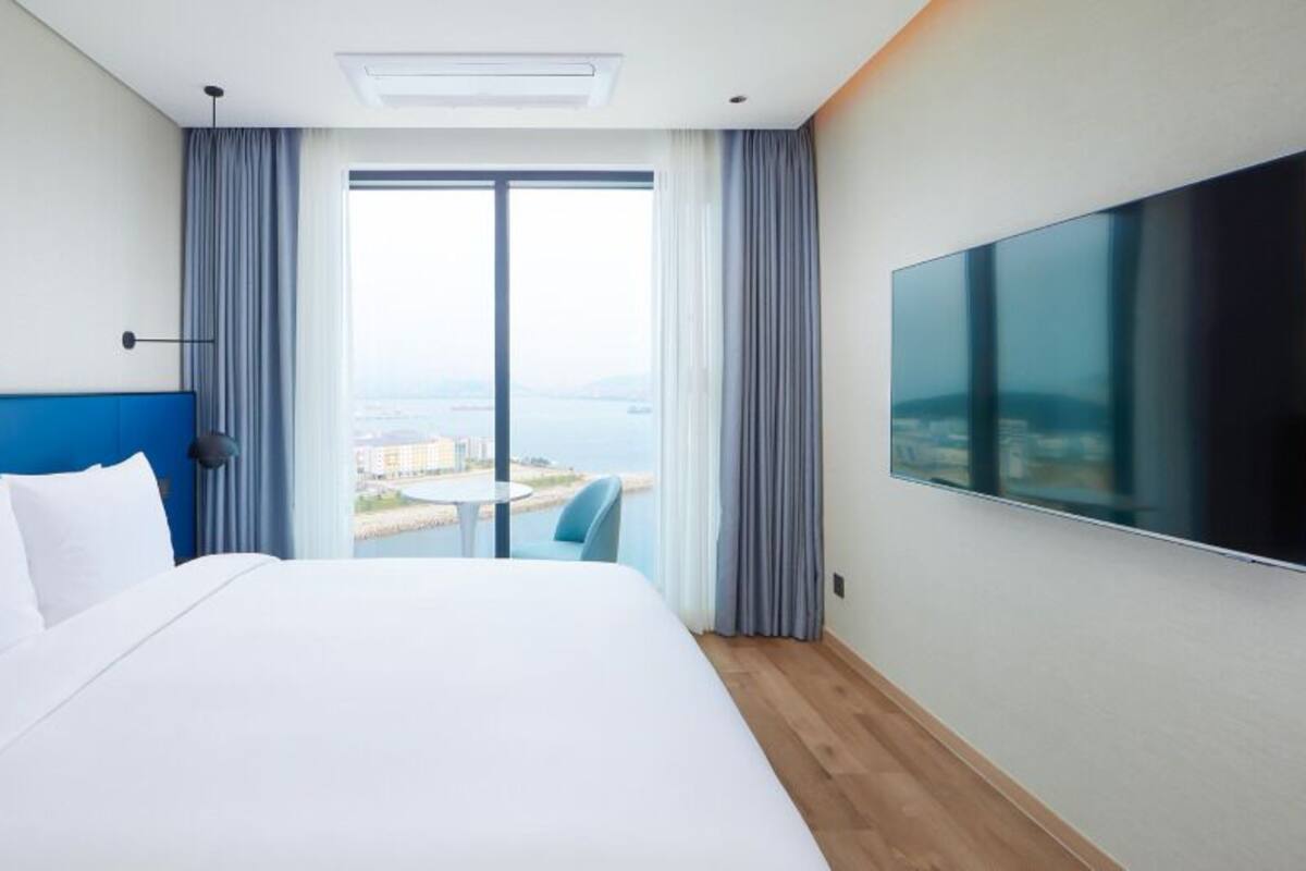Habitación de hotel con una cama grande, un televisor en la pared y vistas a la ciudad por la ventana.