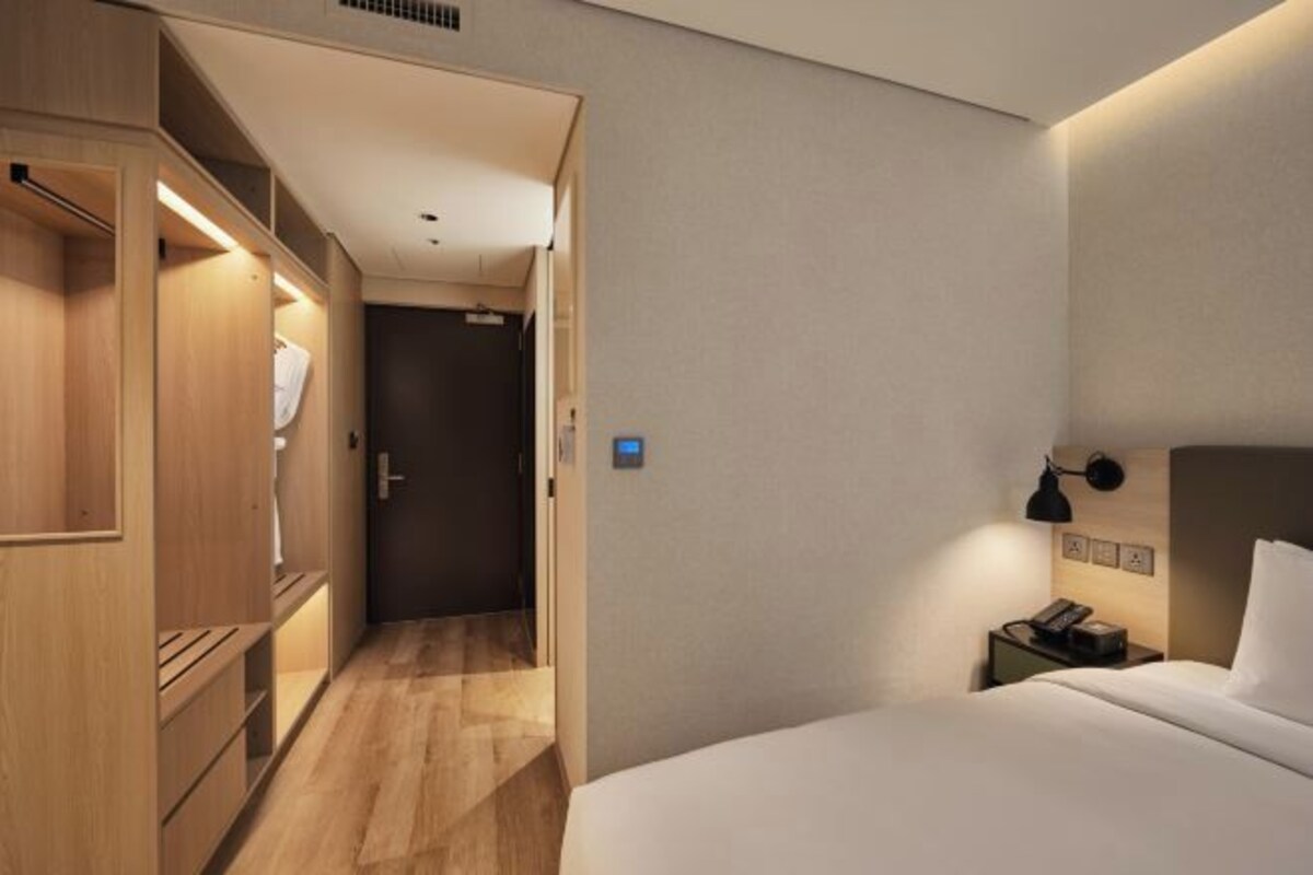 Una habitación de hotel con un armario de madera, una mesita de noche con lámpara y una cama.