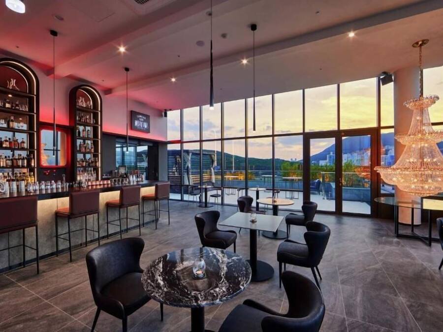 A modern bar area with a large window view, bar stools, and a chandelier.
