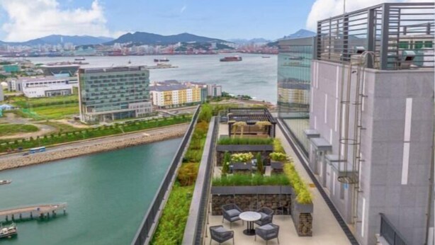 Un hotel moderno con jardín en la azotea, vistas a un río y un paisaje urbano de fondo.