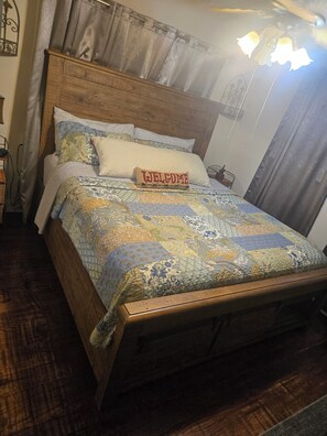 Ein hölzernes Bett mit einer gesteppten Decke, einem Kissen mit der Aufschrift 'WELCOME' und einer Nachttischlampe.