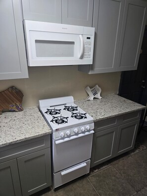 A kitchen with a white stove, a microwave, and a granite countertop.