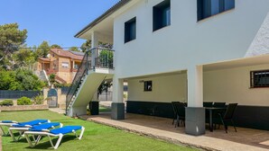 Ein zweistöckiges Gebäude mit überdachter Terrasse, Außenbereich mit Sitzgelegenheiten und einer Treppe zu einer oberen Ebene.