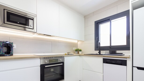 Eine moderne Küche mit weißen Schränken, einem eingebauten Backofen, einer Spülmaschine und einer Mikrowelle.