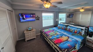 A bedroom with a bed, ceiling fan, TV, dresser, and windows.