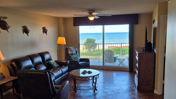 A living room with a leather sofa, a round coffee table, and a view of the ocean through a sliding glass door.