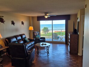 A living room with a leather sofa, a round coffee table, and a view of the ocean through a sliding glass door.