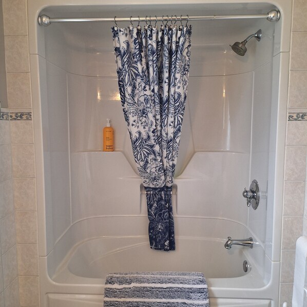 A bathtub with a floral shower curtain, a handheld showerhead, and a bottle of shampoo on the edge. - Relax, Recharge & Reconnect at Amberleigh Guest House (Tichborne)