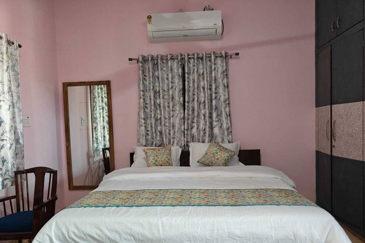 A bedroom with a bed, a chair, a wardrobe, and an air conditioning unit on the wall.