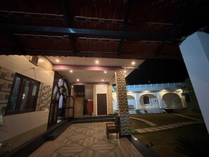 An outdoor covered area with a wooden floor, a bench, and a view of a building with traditional architecture. - Guava resort  (Sawai Madhopur)