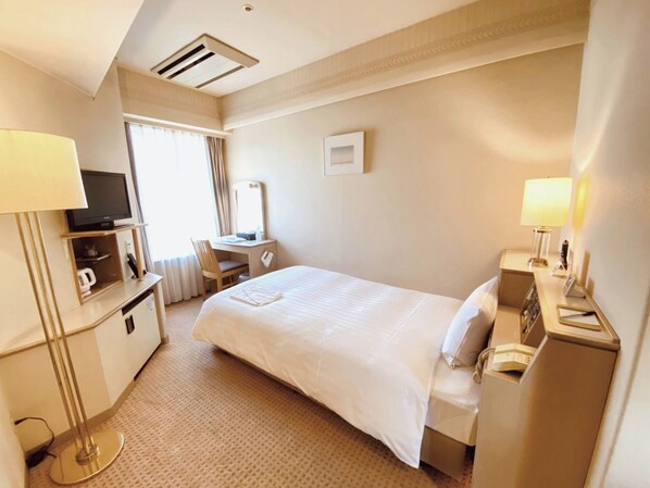 Una habitación de hotel con cama, escritorio, silla, televisor y mesita de noche con lámpara.