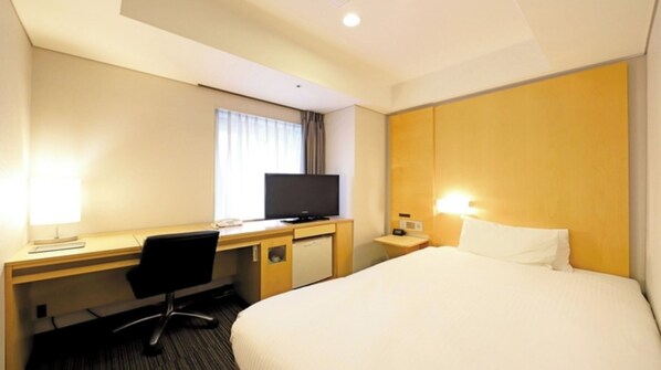 Habitación de hotel con cama, escritorio con silla, televisión, mesita de noche con lámpara y ventana con cortinas.