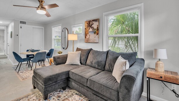 A modern living room with a sectional sofa, dining table, chairs, and a ceiling fan. - Walk to Lakes & Florida Southern | Pet-Friendly | 2BR, BBQ Patio, Sleeps 4 (Lakeland)
