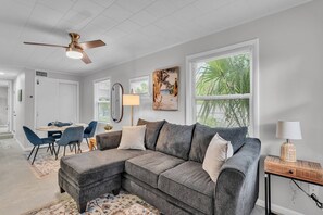 A modern living room with a sectional sofa, dining table, chairs, and a ceiling fan. - Walk to Lakes & Florida Southern | Pet-Friendly | 2BR, BBQ Patio, Sleeps 4 (Lakeland)