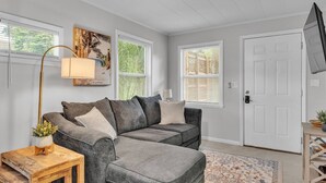 A living room with a gray sectional sofa, a wooden coffee table, a floor lamp, and a patterned rug. - Walk to Lakes & Florida Southern | Pet-Friendly | 2BR, BBQ Patio, Sleeps 4 (Lakeland)
