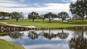 A serene golf course with a pond, stone walls, and trees. - Walk to Lakes & Florida Southern | Pet-Friendly | 2BR, BBQ Patio, Sleeps 4 (Lakeland)