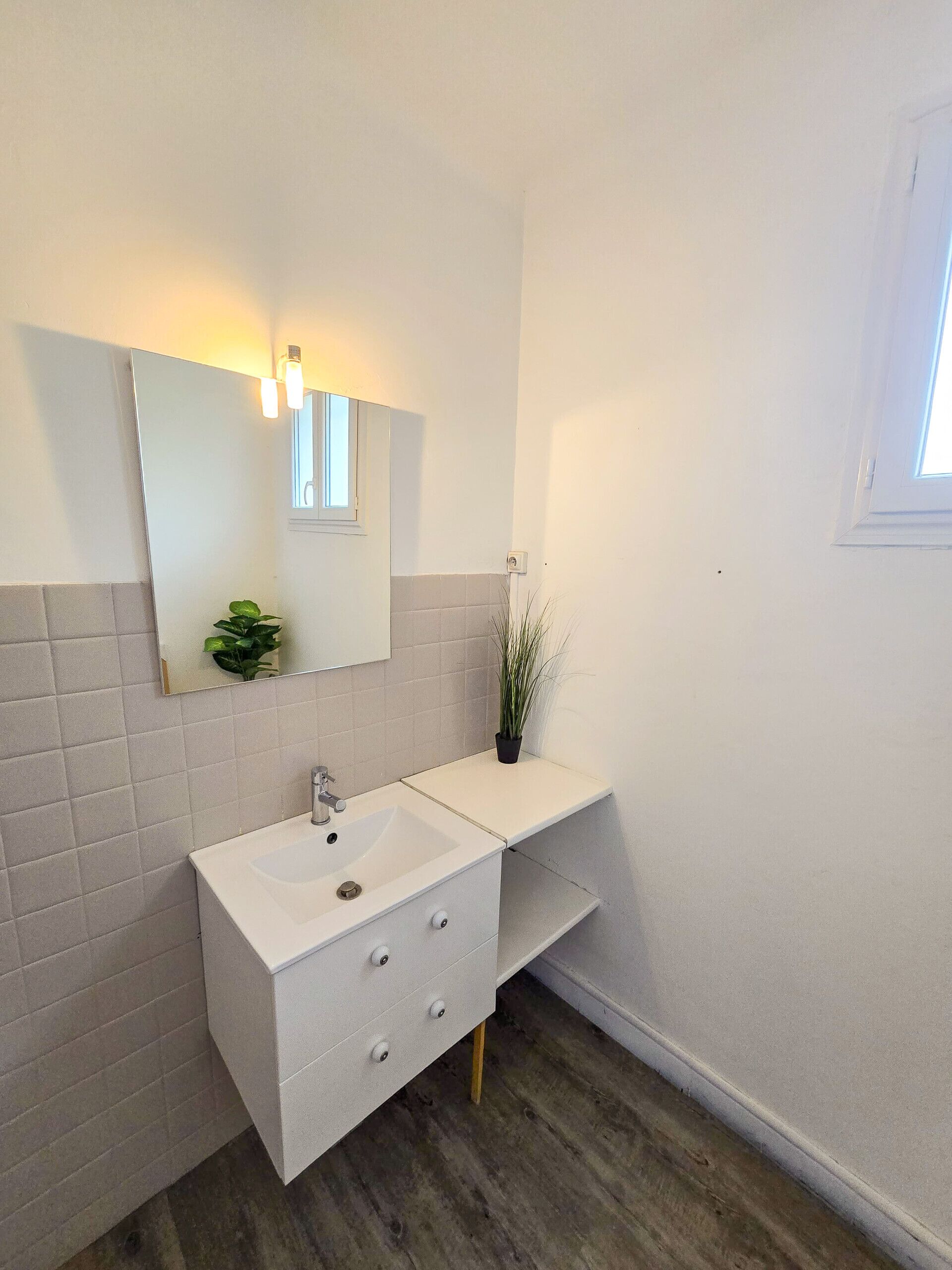 Un baño moderno con lavamanos blanco, espejo y planta en maceta.