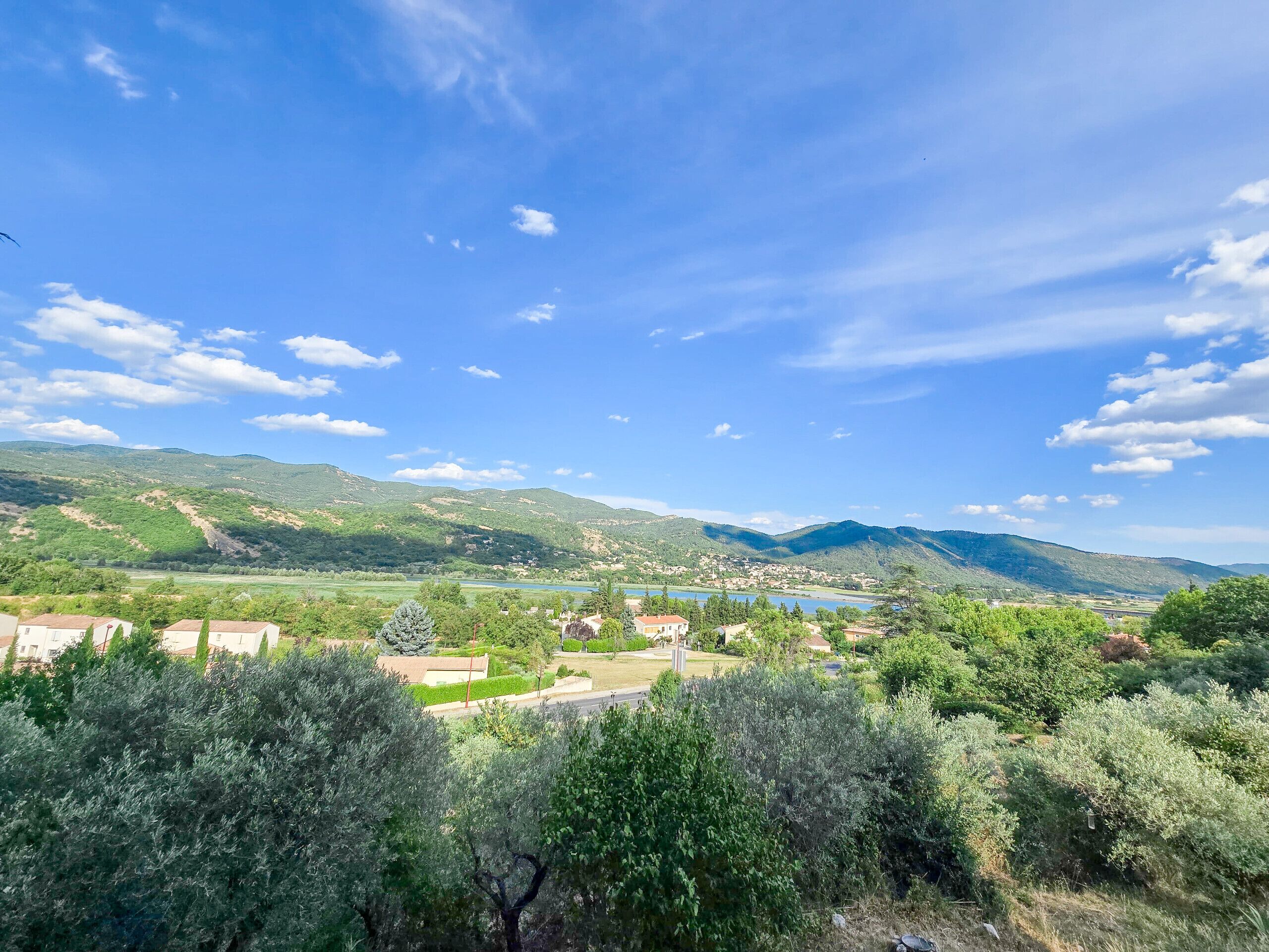 Vista de un pueblo con montañas al fondo, un lago y abundante vegetación en primer plano.
