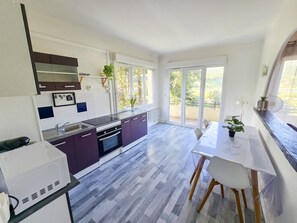 Une cuisine moderne avec un coin repas, de grandes fenêtres et une vue sur l’extérieur.