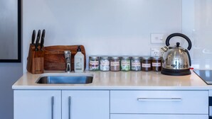 Een keuken met een spoelbak, een waterkoker en verschillende kruidenpotjes op het aanrecht.