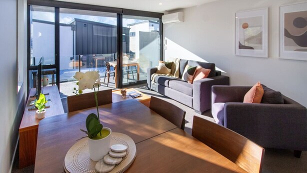 Een moderne woonkamer met een houten eettafel, een bank en een groot raam met uitzicht.
