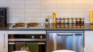 A modern kitchen with a stove, oven, and dishwasher. There are jars of spices and a bottle of oil on the counter.