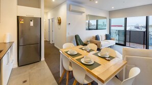 A modern kitchen with a stainless steel refrigerator, a dining area with a wooden table set for four, and a balcony with a city view.